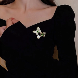 Eleganter Schmetterlings-Perlen-Anstecker mit grünen Steinen an einem schwarzen Blazer