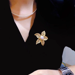 Élégante broche plante à cinq feuilles dorée avec perle centrale sur robe noire