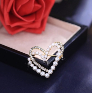 Détail d'une élégante broche cœur dorée avec perles et strass sur un coffret cadeau noir