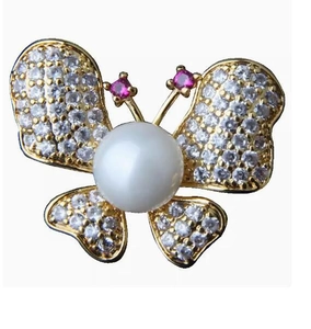 Détail d'une broche papillon dorée avec perle centrale et ailes serties de strass brillants