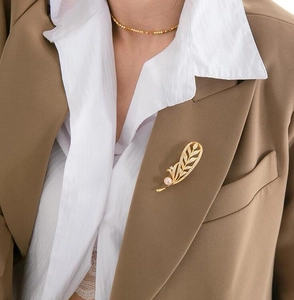 Broche plume dorée élégante avec perle rose et cristaux sur un blazer marron chic