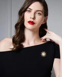 Detail of a gold sunburst brooch with opal stone on a black off-shoulder dress