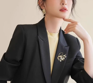 Détail d'une broche cygne dorée ornée de perles blanches sur le revers d'un tailleur noir