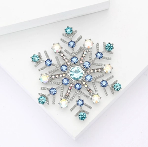 Makro-Detail der Schneeflocken-Brosche mit blauen Strasssteinen auf weißem Podest