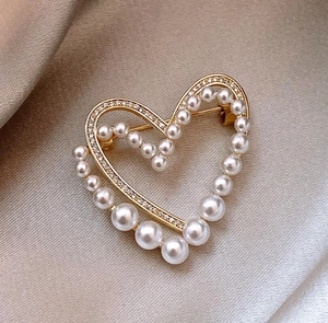 Détail d'une broche cœur dorée élégante avec perles blanches et zircons sur satin