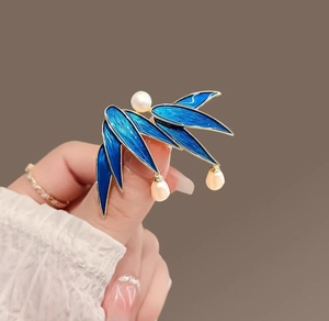 Macro shot of bamboo leaf brooch featuring blue enamel finish and white pearl pendants
