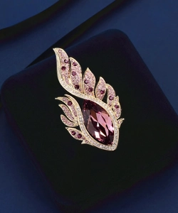 Vue macro d'une broche plume dorée avec cristal violet sur un support en velours bleu