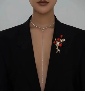 Close-up of elegant gold branch brooch with red berries and Y-shaped silver necklace
