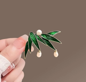 Detail of green bamboo leaf brooch with pearls and gold edges on a solid background