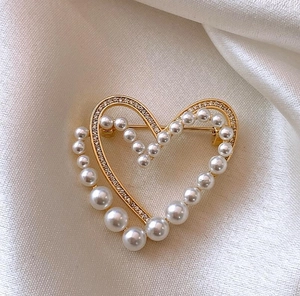 Détail d'une élégante broche cœur dorée avec perles blanches et strass brillants