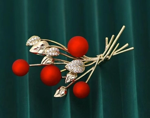 Detail of elegant gold branch brooch with matte red berries and white zircon leaves
