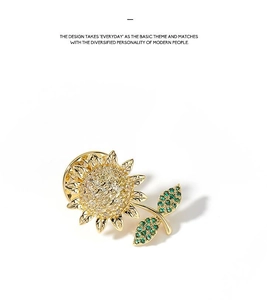 Macro view of gold sunflower brooch pin with green crystal leaves on white background