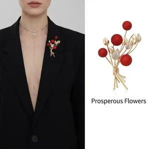 Elegant floral gold brooch with red matte beads and crystal leaves on a black blazer