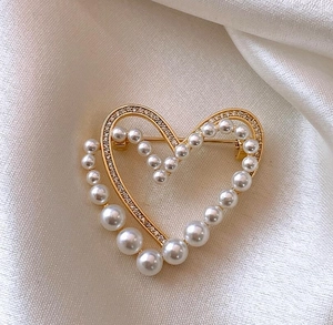 Gros plan détaillé d'une broche en forme de cœur doré avec perles élégantes et strass brillants