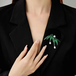 Close-up of a green bamboo leaf brooch with white pearls on a black blazer jacket