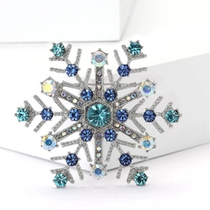 Eleganter silberner Schneeflocken-Anstecker mit blauen Kristallen auf weißer Bühne