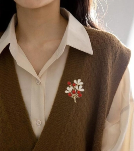 Macro shot of a red fruit plant brooch with gold plating on a brown knitted vest
