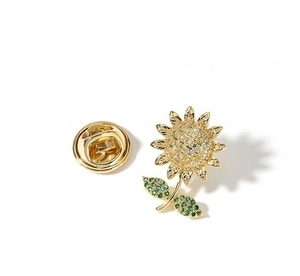 Detail of sunflower brooch with yellow zircons and green leaves on a white background