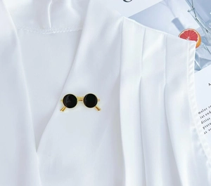Detailed shot of a vintage gold sunglass brooch pinned on white pleated fabric accessory