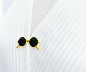 Detail of vintage gold sunglasses brooch with black lenses on white pleated fabric
