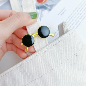 Close-up of a vintage gold sunglasses brooch pinned to a canvas bag strap as a chic accessory