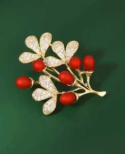 Elegant gold brooch with red berries and rhinestones on a dark green background