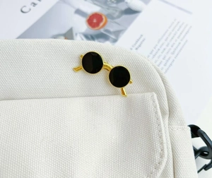 Detail view of a vintage gold sunglasses brooch pinned on a white canvas backpack pocket