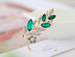 Macro detail of a golden floral branch brooch with emerald stones and white crystals