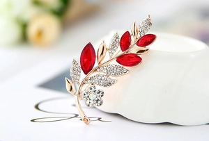 Macro detail of rose gold leaf brooch with red marquise stones and sparkling crystals