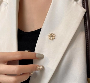 Détail d'une broche fleur en pierre œil-de-chat et strass sur le revers d'un blazer
