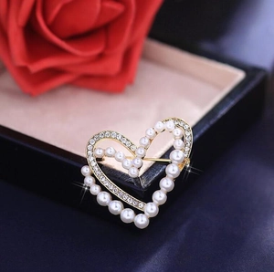 Broche cœur dorée élégante avec perles et cristaux placée près d'une rose rouge