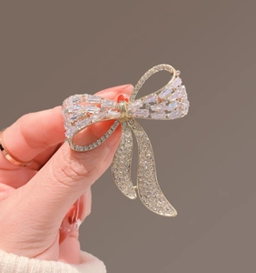 Macro detail of luxury gold bow brooch featuring baguette-cut crystals held in hand