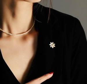 Détail d'une broche marguerite élégante en œil de chat et collier de perles sur un blazer noir