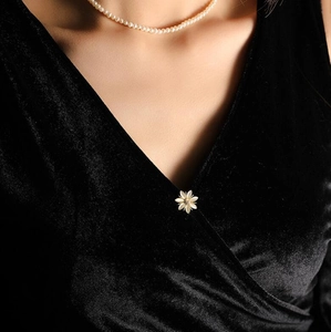 Détail d'une broche marguerite sur une robe en velours noir avec collier de perles