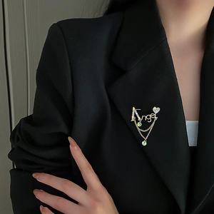 Détail de la broche lettre Angel avec strass et pompons verts sur un costume noir