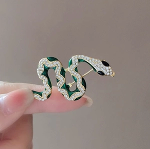 Green enamel and crystal encrusted gold snake brooch held between fingers
