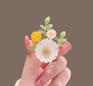 Close-up of daisy flower brooch with pearl luster petals and green enamel leaf details