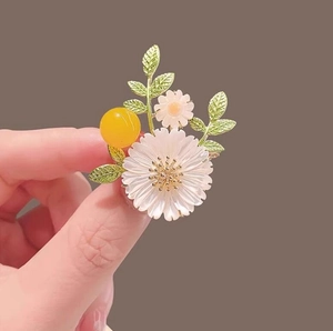 Detailed close-up of white daisy brooch with green leaves and a yellow resin bead