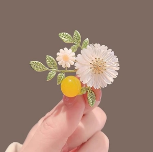 Charming daisy flower brooch with white petals and green leaves held by hand