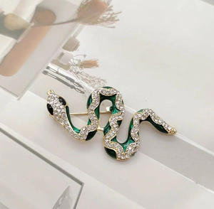 Detailed close-up of emerald green enamel snake brooch with sparkling white rhinestones