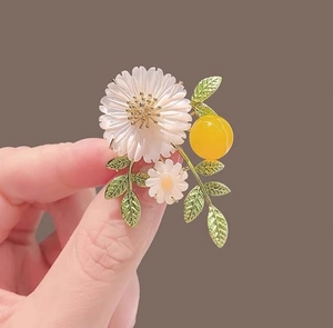 Detail of white daisy brooch with green leaves and yellow fruit on a brown backdrop