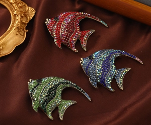 Detail von drei Fischbrosche mit bunten Strasssteinen auf Seidenstoff mit Vintage-Rahmen
