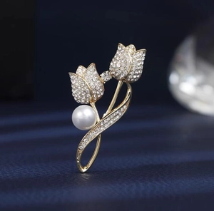 Détail d'une élégante broche tulipe dorée avec strass scintillants et perle blanche