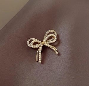 Primer plano de broche de lazo dorado con perlas blancas y diamantes en tela marrón