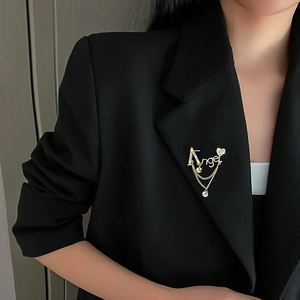 Détail de la broche Angel avec strass et pampilles en cristal vert sur un blazer noir