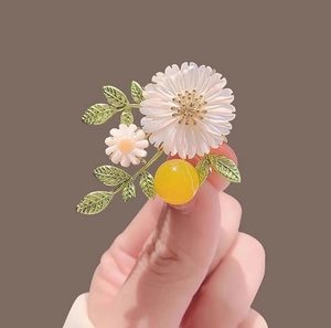 Detail of daisy flower brooch with white shell petals and green enamel leaves