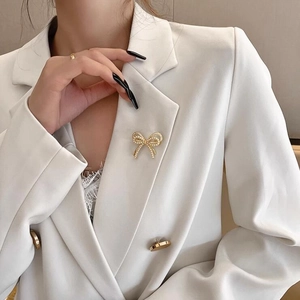 Primer plano de un elegante broche de lazo dorado con perlas blancas en una chaqueta