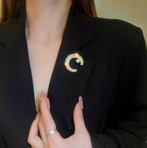 Détail d'une broche en C dorée avec perles blanches et cristaux sur un blazer noir