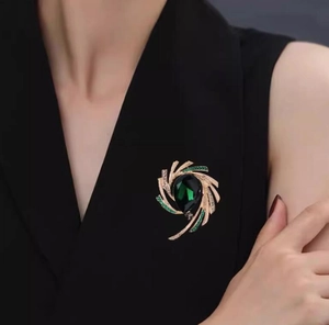 Detail of a vintage golden brooch with a green teardrop stone on a black blazer