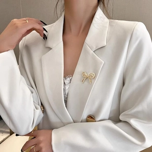 Primer plano de un broche de lazo dorado con perlas en la solapa de un blazer blanco